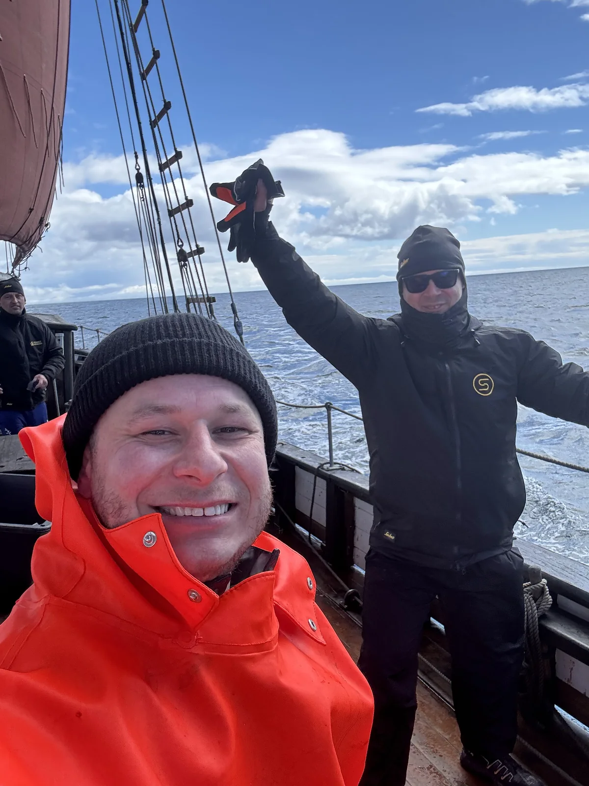 Two people in STERK jackets smiling on the deck of a Faroese sailing vessel at sea