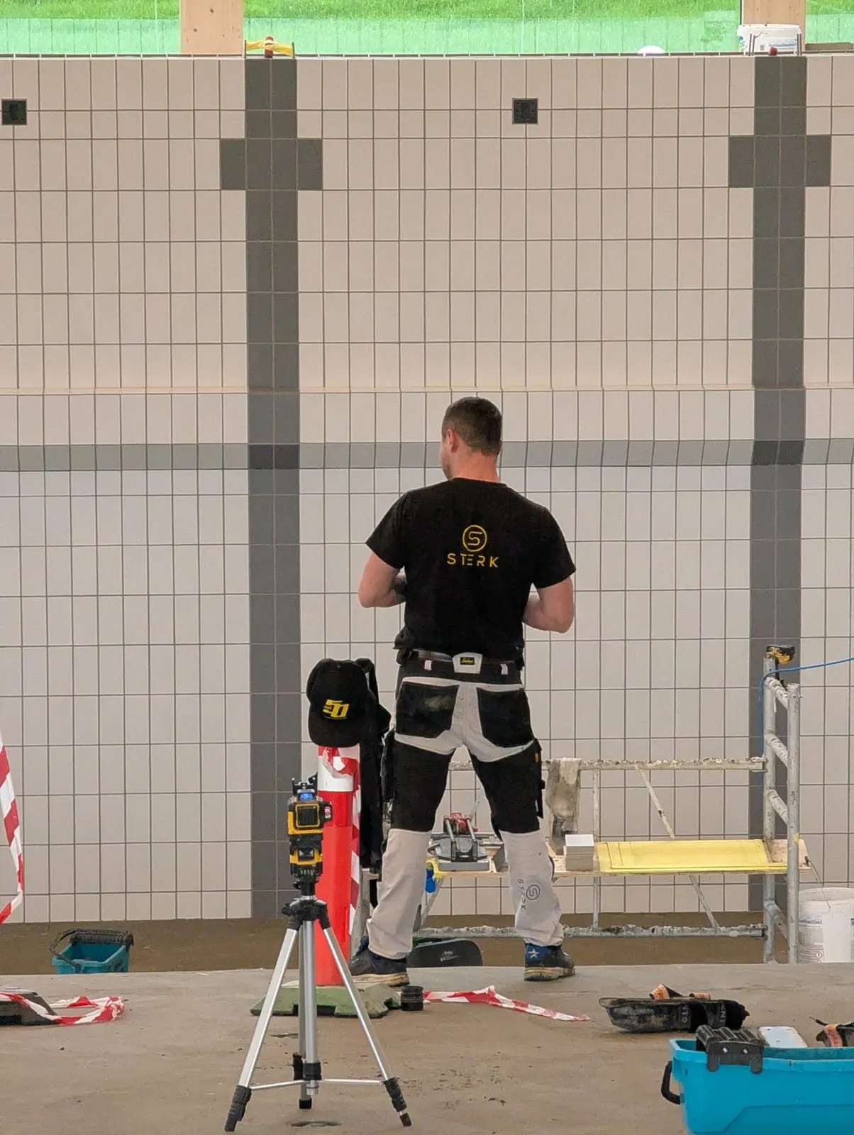 STERK worker in branded workwear tiling the pool wall at Bylgjan